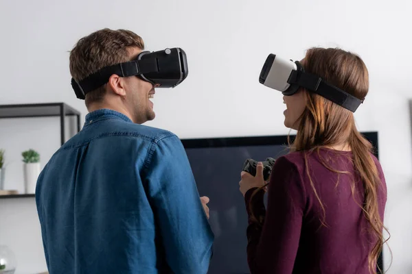 KYIV, UKRAINE - MAY 15, 2020: cheerful couple in virtual reality headsets playing video game in living room — Stock Photo