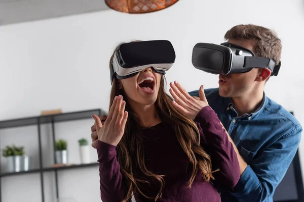 Chica excitada gesto cerca del hombre en auriculares de realidad virtual - foto de stock