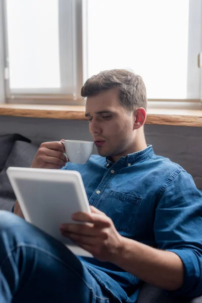 Messa a fuoco selettiva di bello uomo in possesso di tazza e guardando tablet digitale — Foto stock