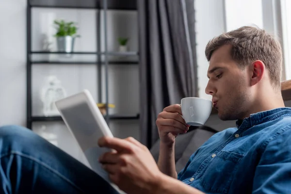 Селективный фокус красивого мужчины с чашкой и цифровым планшетом — стоковое фото