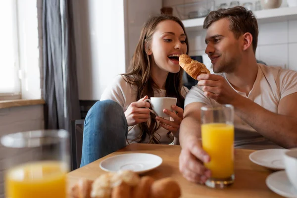 Foco seletivo de homem feliz alimentando menina alegre com croissant saboroso — Fotografia de Stock