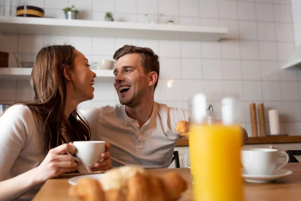 Foco seletivo de mulher feliz e homem olhando uns para os outros perto do café da manhã na cozinha — Fotografia de Stock