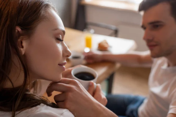 Foco seletivo da mulher com olhos fechados segurando xícara de café perto do namorado — Fotografia de Stock