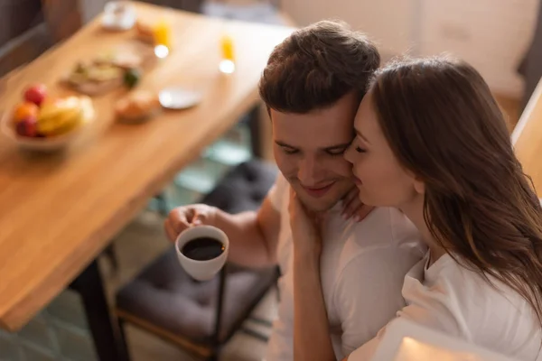 Selektiver Fokus einer jungen Frau, die Mann mit Tasse Kaffee küsst — Stockfoto