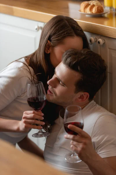 Selektiver Fokus der Frau, die den Mann auf die Wange küsst und ein Glas mit Rotwein hält — Stockfoto