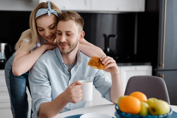 Foco seletivo da menina bonita tocando namorado alegre com xícara de café e croissant na cozinha — Fotografia de Stock