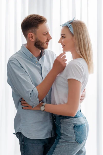 Side view of happy girlfriend and bearded boyfriend looking at each other while hugging in kitchen — Stock Photo