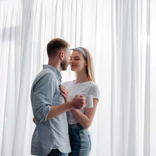 Cheerful woman hugging bearded boyfriend with cup of coffee — Stock Photo