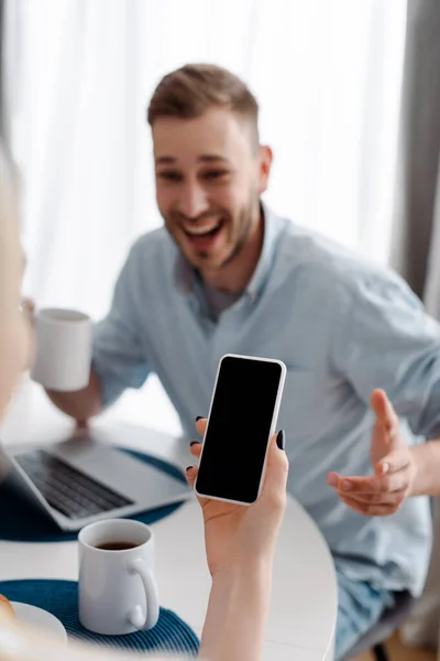 Messa a fuoco selettiva di ragazza che tiene smartphone con schermo bianco vicino allegro fidanzato freelance — Foto stock