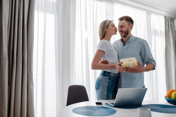 Selective focus of girl holding present and sending air kiss to happy boyfriend — Stock Photo