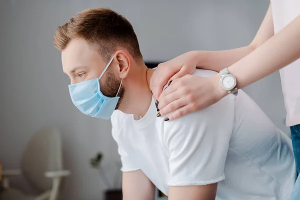 Девушка трогает разочарованного мужчину в медицинской маске дома — стоковое фото