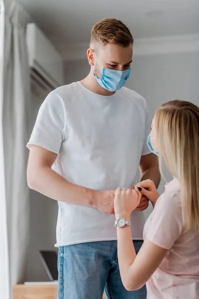 Женщина и мужчина в медицинских масках держатся за руки дома — стоковое фото