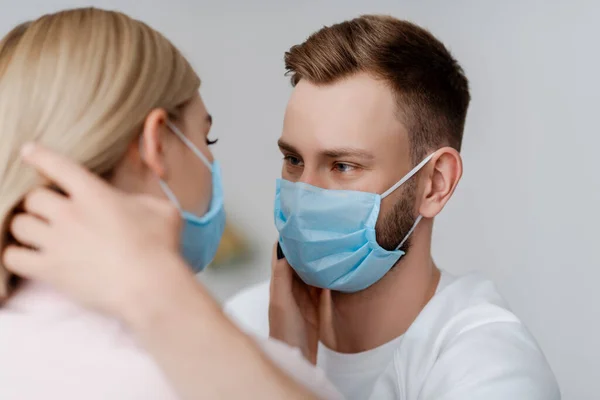 Selective focus of man in medical mask touching hair of young woman at home — Stock Photo