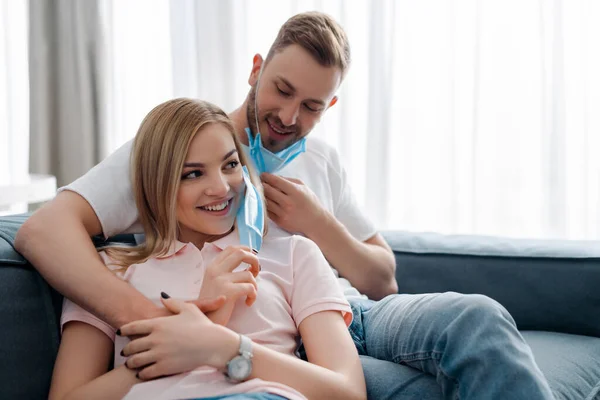 Щасливий чоловік і дівчина в медичних масках посміхаються у вітальні — стокове фото