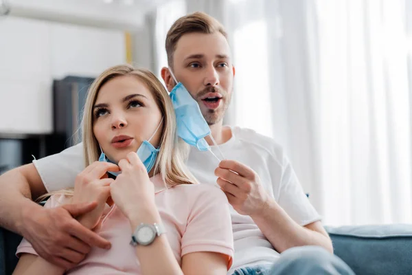 Schöner Mann und attraktives Mädchen berühren medizinische Masken und atmen zu Hause erleichtert auf — Stockfoto