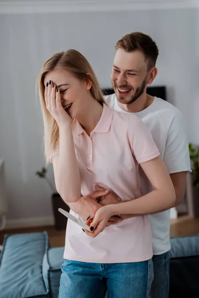 Happy man hugging pregnant girlfriend holding pregnancy test with positive result — Stock Photo