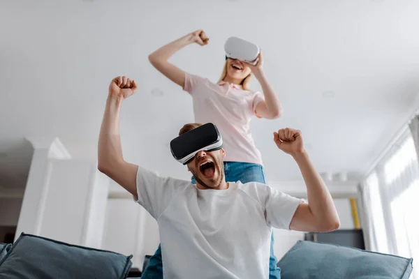 Selective focus of excited couple in virtual reality headsets gaming and celebrating triumph at home — Stock Photo