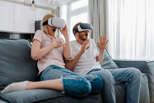 Scared couple in virtual reality headsets gaming at home — Stock Photo