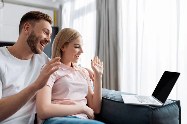 Allegra coppia agitando le mani e guardando il computer portatile con schermo vuoto, pur avendo video chat — Foto stock