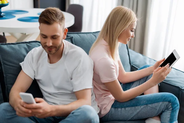 Enfoque selectivo del hombre utilizando el teléfono inteligente cerca de la mujer que sostiene la tableta digital con pantalla en blanco - foto de stock