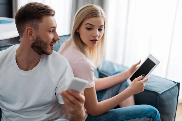 Selective focus of man showing smartphone to woman holding digital tablet with blank screen — Stock Photo