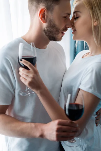 Side view of cheerful man and woman holding glasses with red wine — Stock Photo