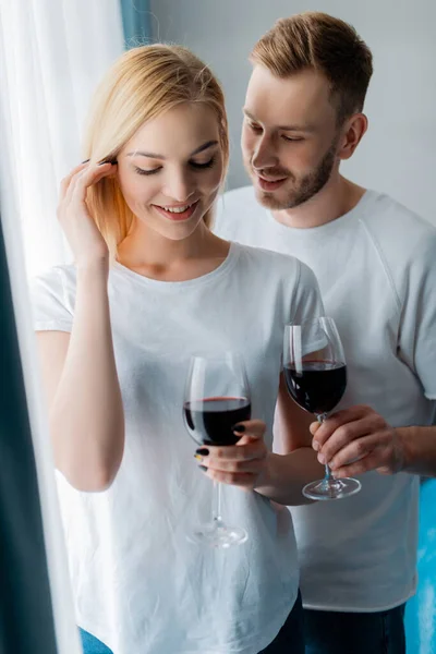 Homem bonito olhando para a mulher e segurando vidro com vinho tinto — Fotografia de Stock