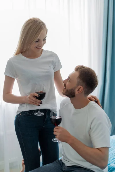 Mujer feliz sosteniendo copa con vino tinto y mirando al hombre - foto de stock