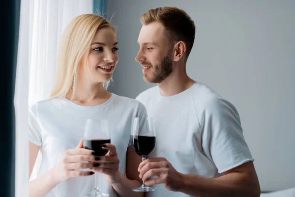 Vista laterale di uomo felice e donna allegra che tiene i bicchieri con vino rosso — Foto stock