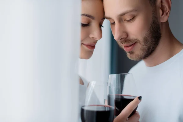 Selective focus of handsome man and beautiful woman holding glasses with red wine — Stock Photo