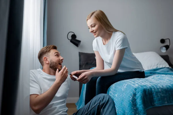 Selektiver Fokus der glücklichen jungen Frau, die einen Schwangerschaftstest mit positivem Ergebnis in der Nähe eines fröhlichen Mannes abhält — Stockfoto