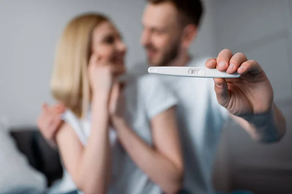 Selektiver Fokus eines glücklichen Mannes, der einen Schwangerschaftstest mit positivem Ergebnis in der Nähe einer fröhlichen Frau abhält — Stockfoto