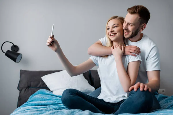 Счастливая молодая пара делает селфи в спальне — стоковое фото