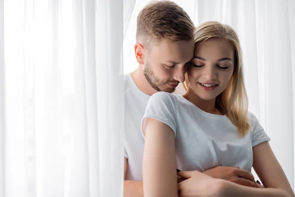 Handsome man embracing beautiful and smiling girl with closed eyes — Stock Photo