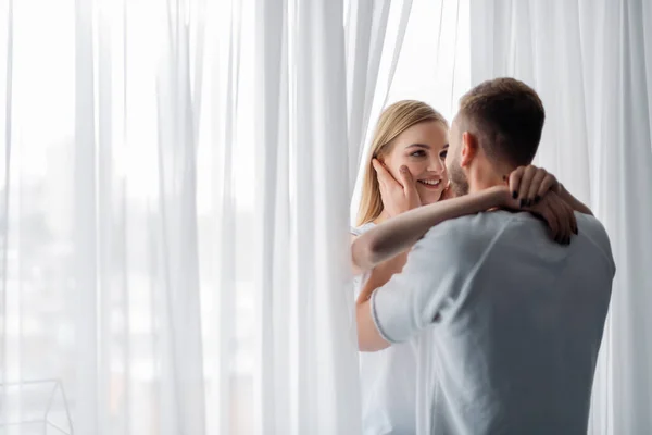 Щаслива жінка посміхається, обіймаючи чоловіка вдома — стокове фото