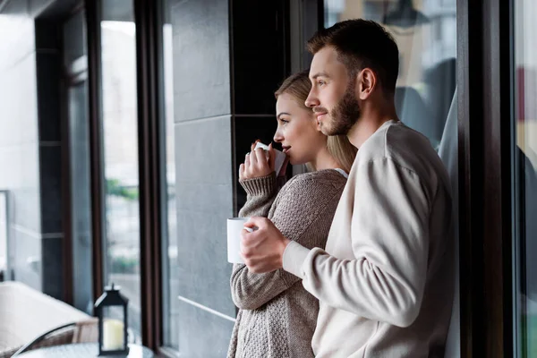 Chica atractiva y hombre guapo sosteniendo tazas de café fuera — Stock Photo