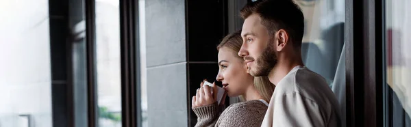 Imagen horizontal de chica atractiva sosteniendo taza de café cerca de hombre guapo afuera - foto de stock