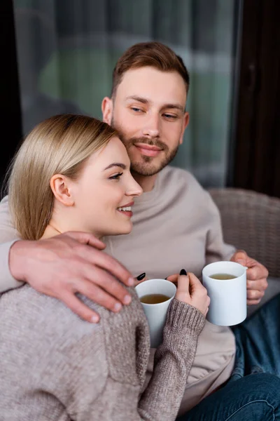 Selektiver Fokus des glücklichen Mannes, der eine Tasse Tee hält und Freundin umarmt — Stockfoto