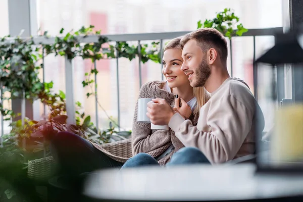 Enfoque selectivo de la pareja feliz sosteniendo tazas mientras está sentado fuera - foto de stock