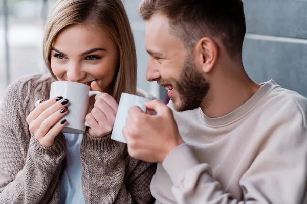 Couple joyeux souriant et tenant tasses avec des boissons — Photo de stock