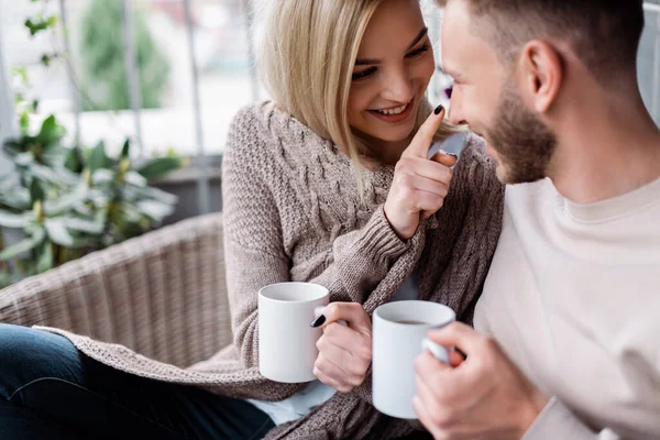 Enfoque selectivo de chica feliz sosteniendo taza y tocando la nariz de novio alegre - foto de stock