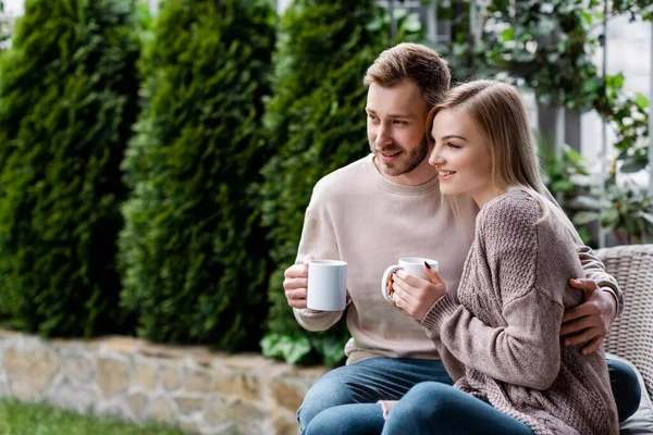 Bel homme et femme gaie tenant des tasses de thé et assis dehors — Photo de stock