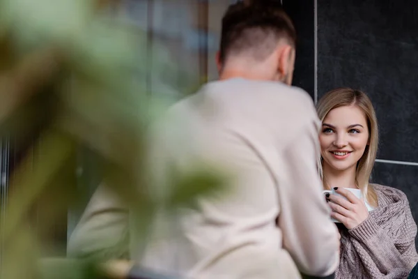 Enfoque selectivo de la mujer feliz sosteniendo la taza y mirando al hombre fuera - foto de stock