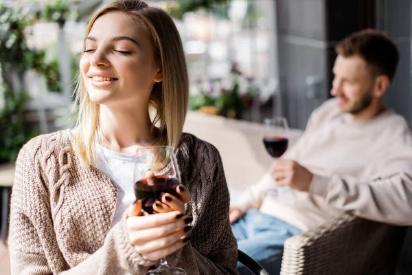 Selektiver Fokus eines fröhlichen Mädchens mit geschlossenen Augen, das ein Glas Rotwein in der Nähe des Mannes hält — Stockfoto