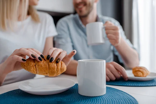 Foco seletivo da mulher segurando croissant perto da placa e do homem com copo — Fotografia de Stock