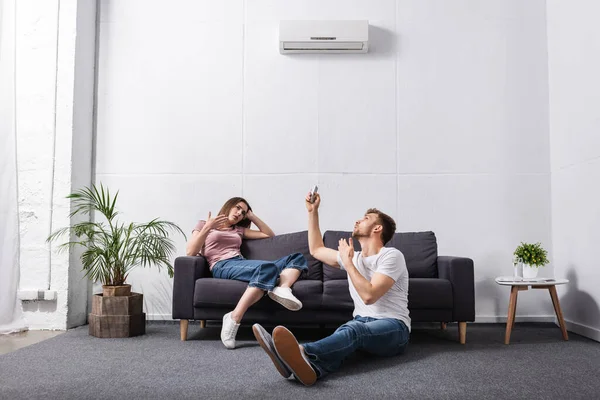 Casal triste com controlador remoto em casa com ar condicionado quebrado — Fotografia de Stock
