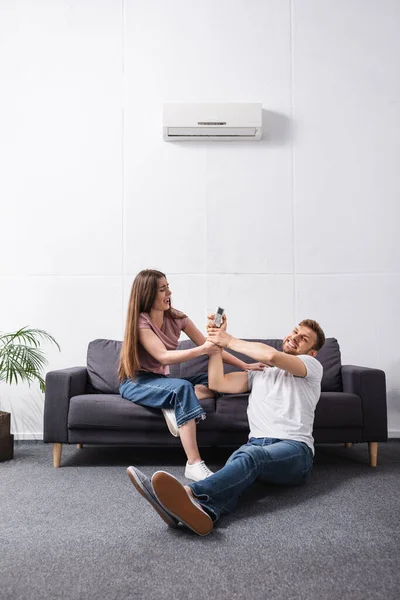 Jeune couple irrité avec télécommande à la maison avec climatiseur cassé — Photo de stock