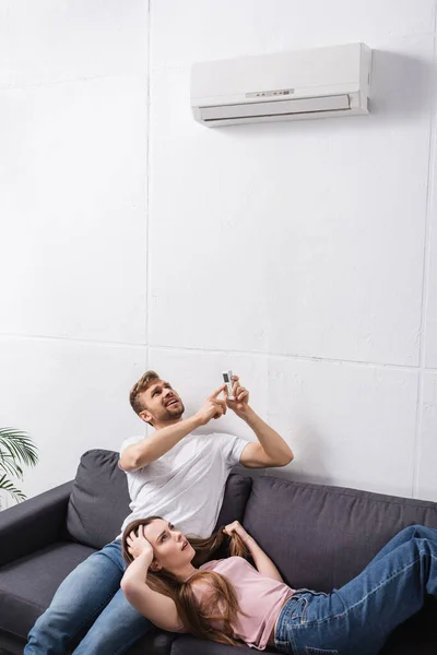 Casal preocupado com controlador remoto sofrendo de calor em casa com ar condicionado quebrado — Fotografia de Stock