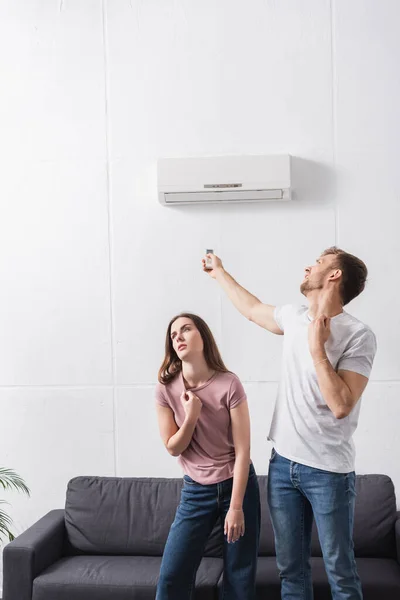 Casal exausto com controlador remoto sofrendo de calor em casa com ar condicionado quebrado — Fotografia de Stock