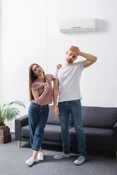 Casal frustrado com ventilador de mão e jornal sofrendo de calor em casa com ar condicionado quebrado — Fotografia de Stock
